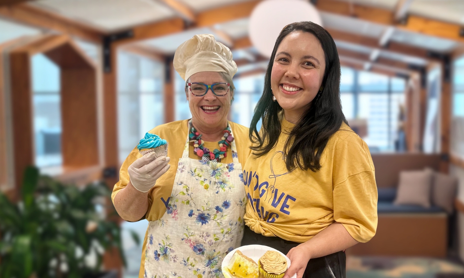 Two people are showing off their baked goods as they smile for a photo together