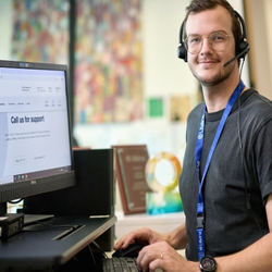A young Crisis Supporter wearing a headset and working at a computer smiles warmly at the camera