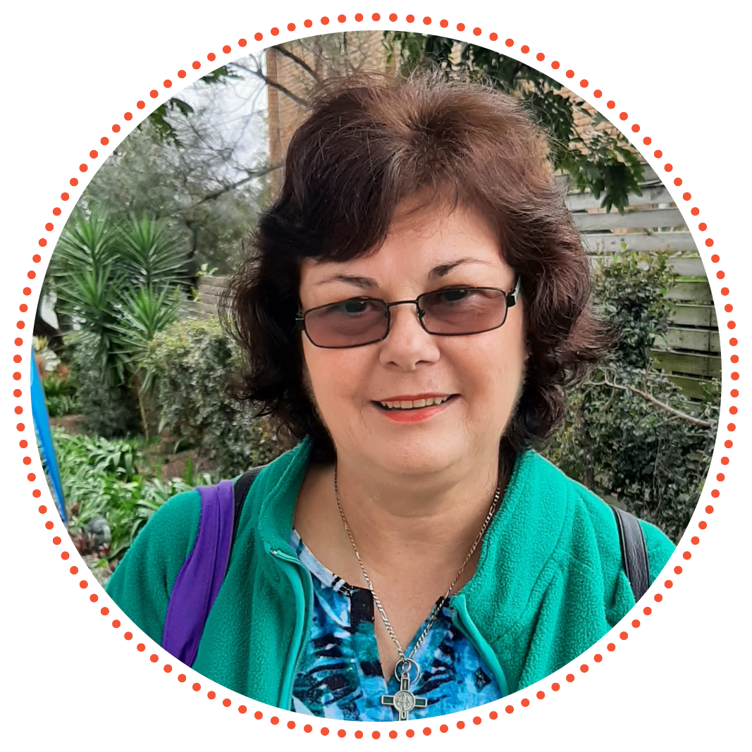 A photo of Amanda. She is smiling warmly and wearing glasses out in a green space.