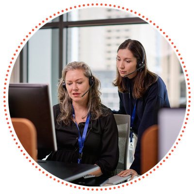 A Crisis Supporter Volunteer and a Calling Coach are wearing headsets and looking at a computer screen in a Crisis Support Centre.
